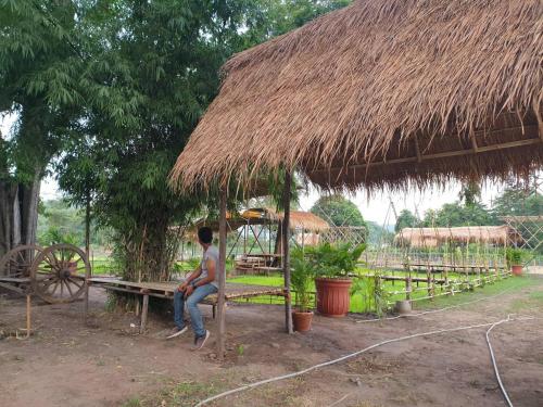 a man sitting on a bench under a straw hut at Supalai Pasak Resort Hotel And Spa in Kaeng Khoi