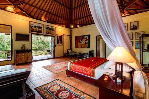 a bedroom with a bed and a couch and a television at Tanah Merah Art Resort in Ubud