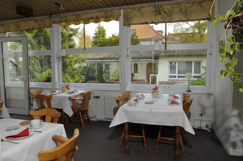 un restaurante con mesas y sillas blancas y ventanas en Hotel Hubertus en Hannover
