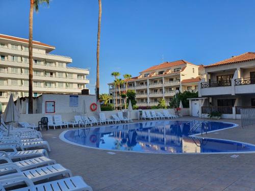 uma piscina com espreguiçadeiras brancas e um hotel em Spectacular Ocean Apartment with AirCon in Golden Mile of Las Americas em Arona
