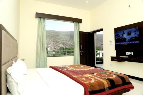 une chambre avec un lit, une télévision et une fenêtre dans l'établissement Aravali Hills Resort, à Pushkar