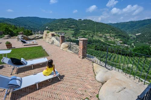 a young girl sitting on a bench on a patio with mountains at Tenuta Pian D'Attesio - Agriturismo in Castelletto Soprano