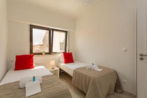 パレーデにあるBeGuest Parede Beach Apartment – Cascaisの赤い枕が付いたベッド2台が備わる客室です。