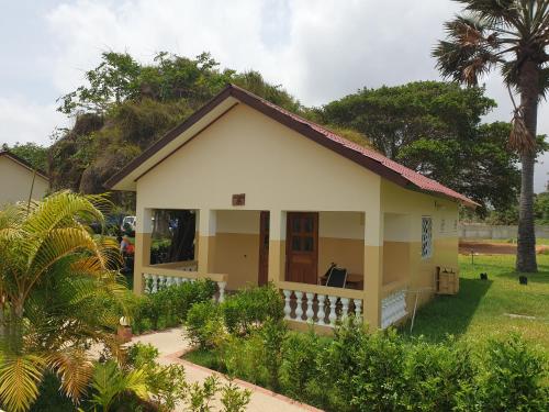 a small yellow and white house with a palm tree at Kunta Kinteh Beach Complex in Kotu