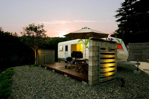 an rv with an umbrella and a wooden deck at Tropical Dream Spa Caravan in Geoje