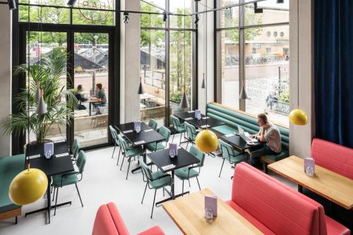 a restaurant with red and green chairs and a person sitting at tables at The Social Hub Eindhoven in Eindhoven
