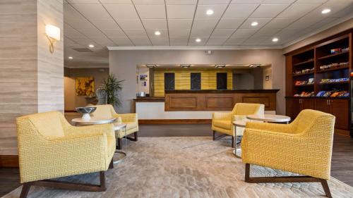 a waiting room with yellow chairs and tables and a counter at Cottonwood Airport & Expo Hotel Louisville in Louisville