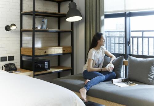 a woman sitting on a couch next to a bed at Just Sleep - Sanchong in Taipei