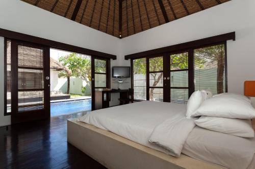 a bedroom with a bed with white sheets and windows at Bvilla Spa in Seminyak