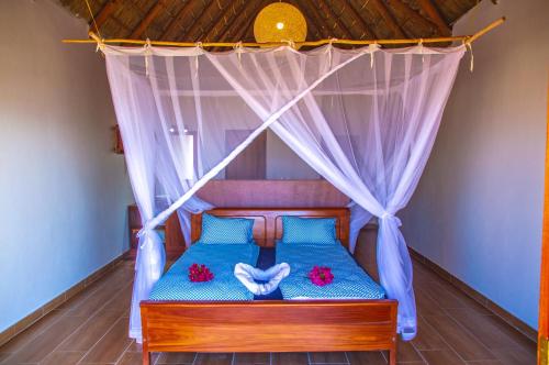 a bedroom with a canopy bed with blue sheets and red flowers at Vilancool Beach Resort in Vilanculos