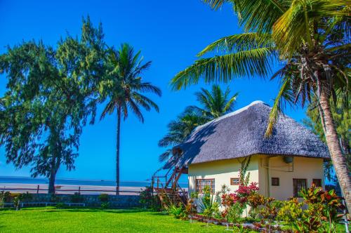 a thatch roofed house with palm trees on the beach at Vilancool Beach Resort in Vilanculos
