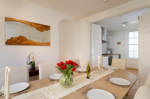 a dining room with a table with red flowers in a vase at Central Brighton Town House by MyHolidayLet in Brighton & Hove