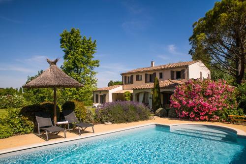 une piscine avec deux chaises et un parasol ainsi qu'une maison dans l'établissement Auberge De Garance - Villa Prestige 5 Étoiles & Table Gastronomique Étoilé, à Saint-Rémy-de-Provence