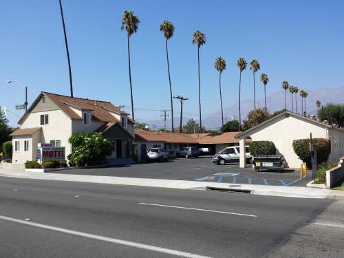 een straat met auto's geparkeerd op een parkeerplaats met palmbomen bij New Kansan Motel in Rancho Cucamonga
