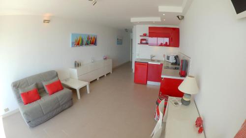 un salon avec un canapé et une cuisine avec des placards rouges dans l'établissement Front de mer T2 PALAVAS LES FLOTS direct plage, à Palavas-les-Flots