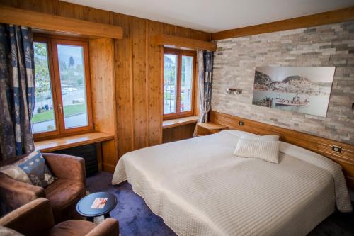 a bedroom with a bed and a chair and windows at HOTEL de la Truite & SPA Le petit Nautilus in Le Pont