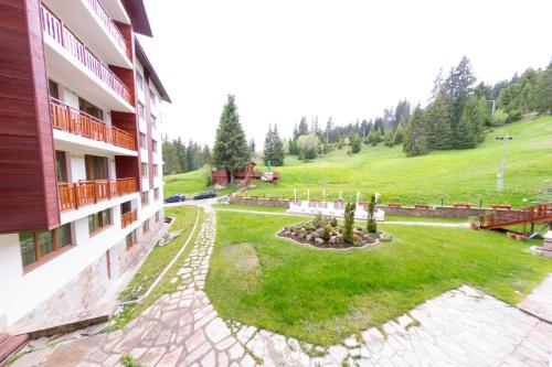 a building with a yard next to a green hill at Forest Nook Aparthotel in Pamporovo