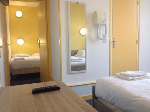 a room with two beds and a table and a mirror at Hotel Couleurs Sud Centre-ville Gare Charleville-Mézières in Charleville-Mézières