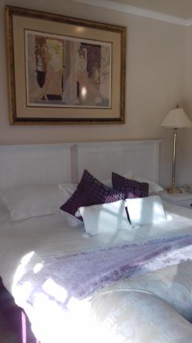 a white bed with purple pillows on top of it at Mulligans Guest Lodge in Hermanus