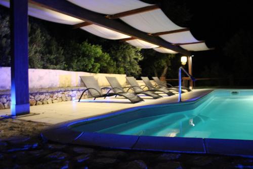 um grupo de cadeiras sentadas ao lado de uma piscina à noite em La Quercia em Arbus