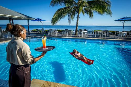a woman holding a tray with a drink in a swimming pool at Heritage Park Hotel in Honiara