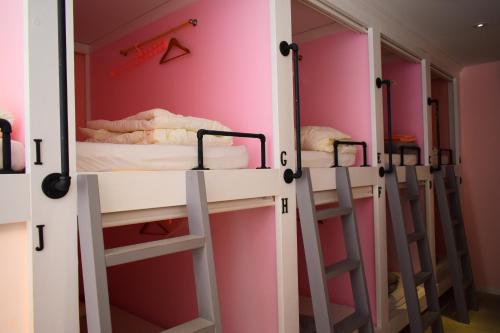 a row of bunk beds in a room with pink walls at ラナイ ホテルアンドドミトリー in Naha
