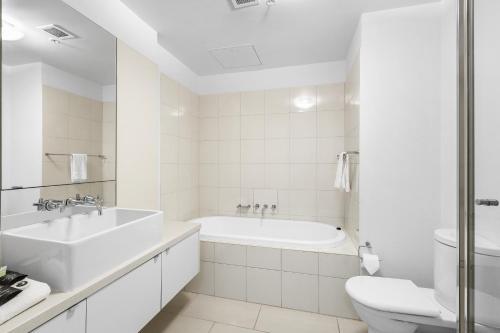 a white bathroom with a tub and a sink and a toilet at Melbourne Holiday Apartments Flinders Wharf in Melbourne