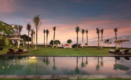 a pool with palm trees and a sunset in the background at WakaGangga in Tabanan