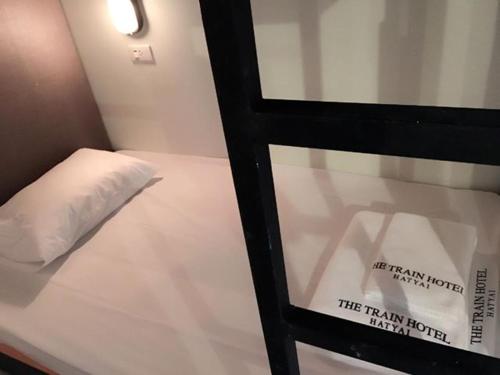 a bed with a pillow and a sign on a window at The Train Hotel Hatyai in Hat Yai