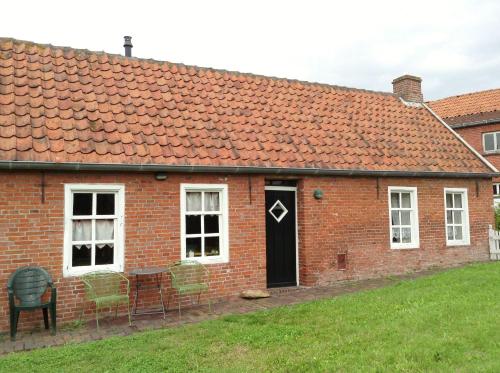 a red brick house with a black door and chairs at Jabjemööh's Huus in Greetsiel