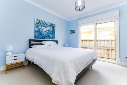 a blue bedroom with a large bed and a window at WALKIN ON SUNSHINE - STROLL TO BEACH BREAK in Inverloch
