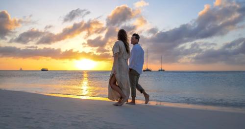 a man and woman walking on the beach at sunset at Barceló Aruba - All Inclusive in Palm-Eagle Beach