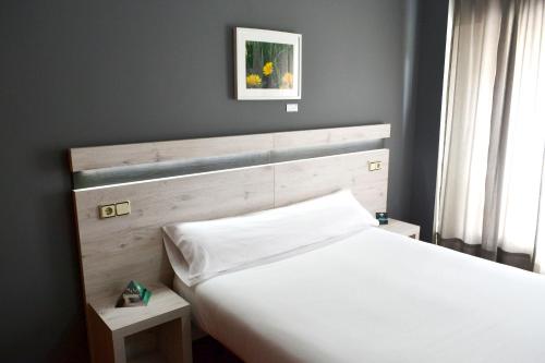 ア・コルーニャにあるAlda Puerta Coruñaの白いベッド1台(木製ヘッドボード付)が備わるベッドルーム1室が備わります。