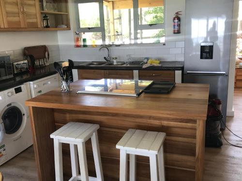 a kitchen with a wooden island with two white stools at Trinity Farm Ocean view Cottage in Plettenberg Bay