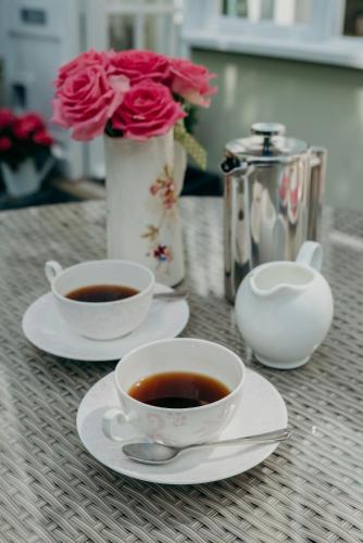 two cups of coffee on a table with a vase with roses at Apple Tree Bed and Breakfast in Tavistock