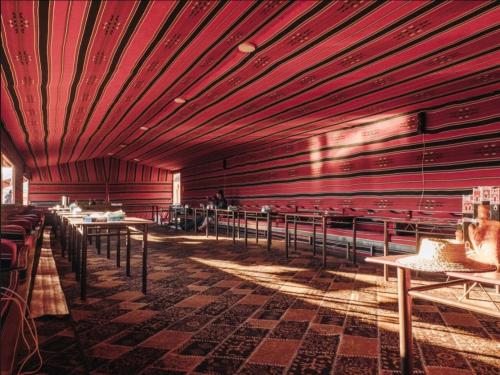 a dining room with red walls and tables and chairs at Wadi Rum Moon Camp in Wadi Rum