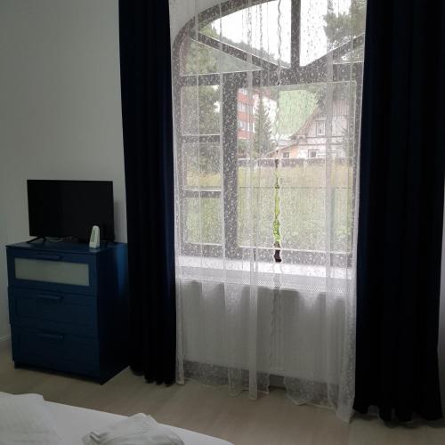 a bedroom with a window with white curtains and a tv at White Wood Chalet in Buşteni