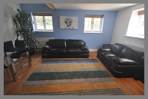 a living room with a black leather couch and a rug at Court Farm Barns in Warborough