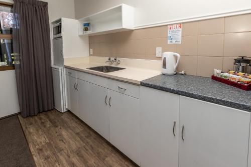 a kitchen with white cabinets and a sink at ASURE Explorer Motel & Apartments in Te Anau