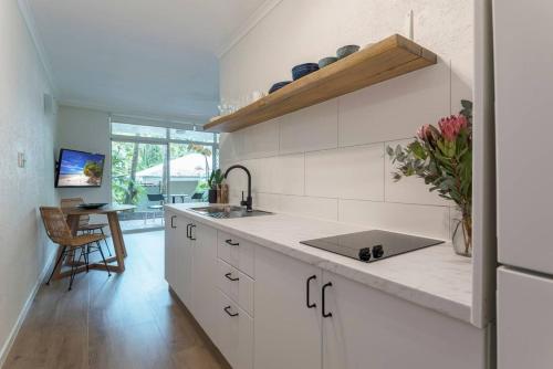 a kitchen with white cabinets and a sink and a table at Ocean Palms Apartments in Port Douglas