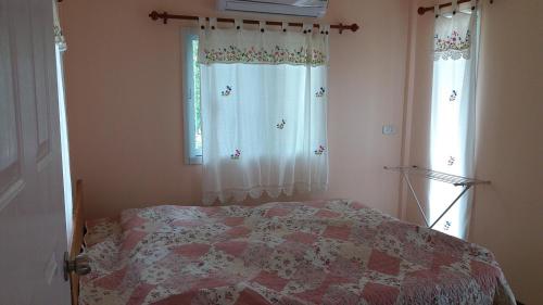a bedroom with a bed and two windows with curtains at Tarmtawan garden home in Nakhon Nayok