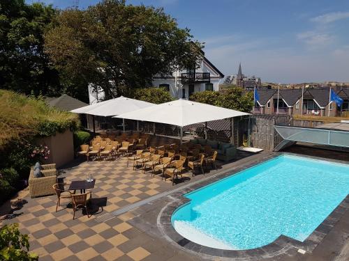 a swimming pool with chairs and a table and an umbrella at Boutique hotel Puur Zee - Adults Only in Wijk aan Zee