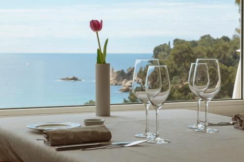 
three wine glasses sit on a table with a view of the ocean at Hotel Santa Marta in Lloret de Mar
