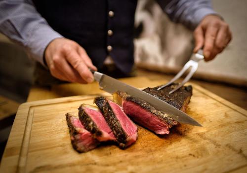 a person cutting meat on a cutting board with a knife at Neo Hotel Linde Esslingen in Esslingen
