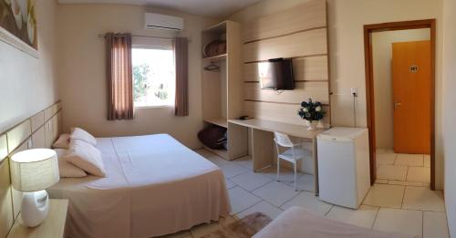 a bedroom with a bed and a desk and a window at Hotel Do Santo in Giruá