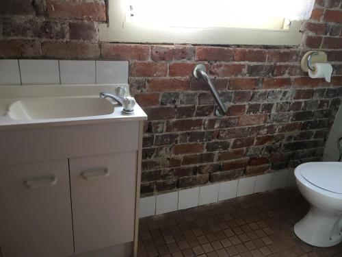 a bathroom with a white sink and a brick wall at Centennial Hotel Gulgong in Gulgong