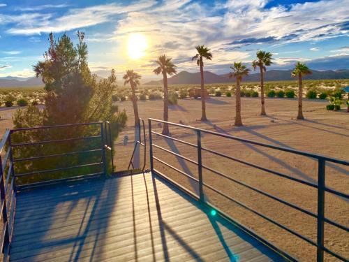 a boardwalk with palm trees and the sun in the distance at The Castle House Estate in Joshua Tree