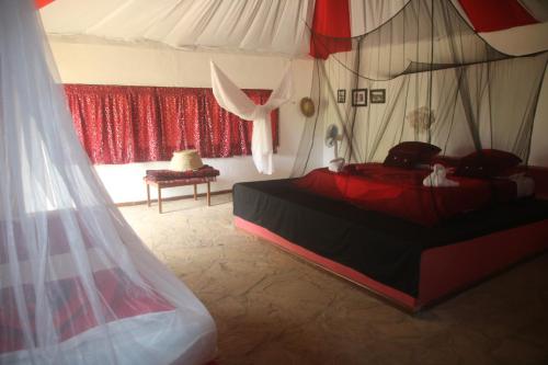 a bedroom with a bed with a red and white canopy at Gecko Nature Lodge Home of Swahili Divers the BEST dive center and Famous Gecko Restaurant in Verani