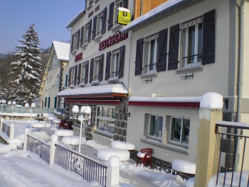 a building with snow on the ground in front of it at Logis Hôtel Le Beau Site in Chambon-sur-Lac