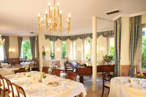 una sala da pranzo con tavoli, sedie e lampadario a braccio di Hotel Villa Meererbusch a Meerbusch